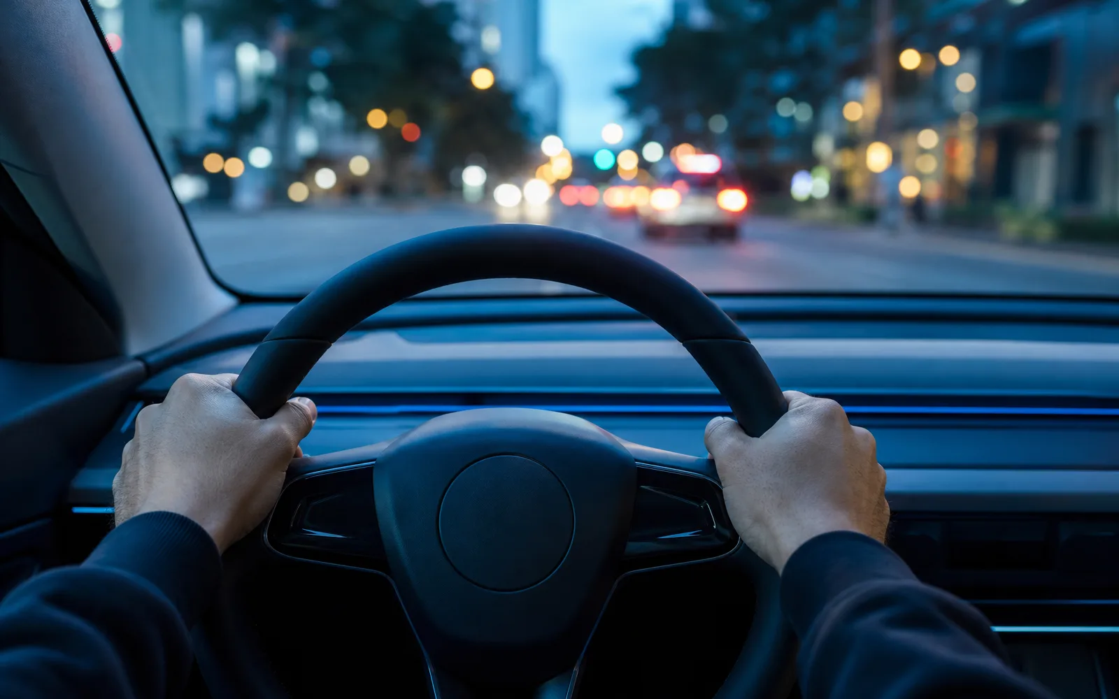 Mãos ao volante de um carro moderno com a cidade ao fundo pelo para-brisa